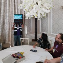 A person holds up a laptop for others to see what to copy – blindfolded!