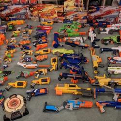 Many nerf guns in a wide variety of colours, laid out on the floor.