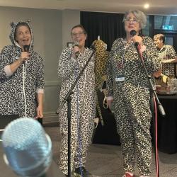 3 people in leopard onsies singing with microphones. 